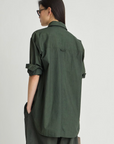 Dark green organic cotton Apiece Apart oversized button down, shown from behind on person with glasses.