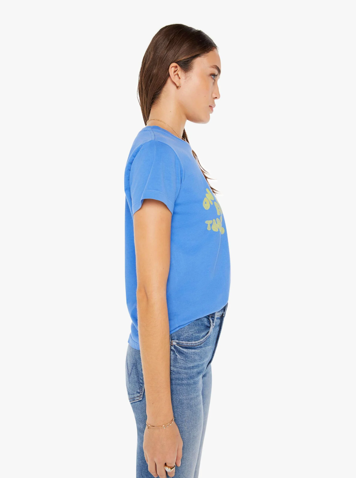 Side profile of a woman wearing The Boxy Goodie Goodie On The Road Again blue t-shirt with text and blue jeans, standing against a white background.