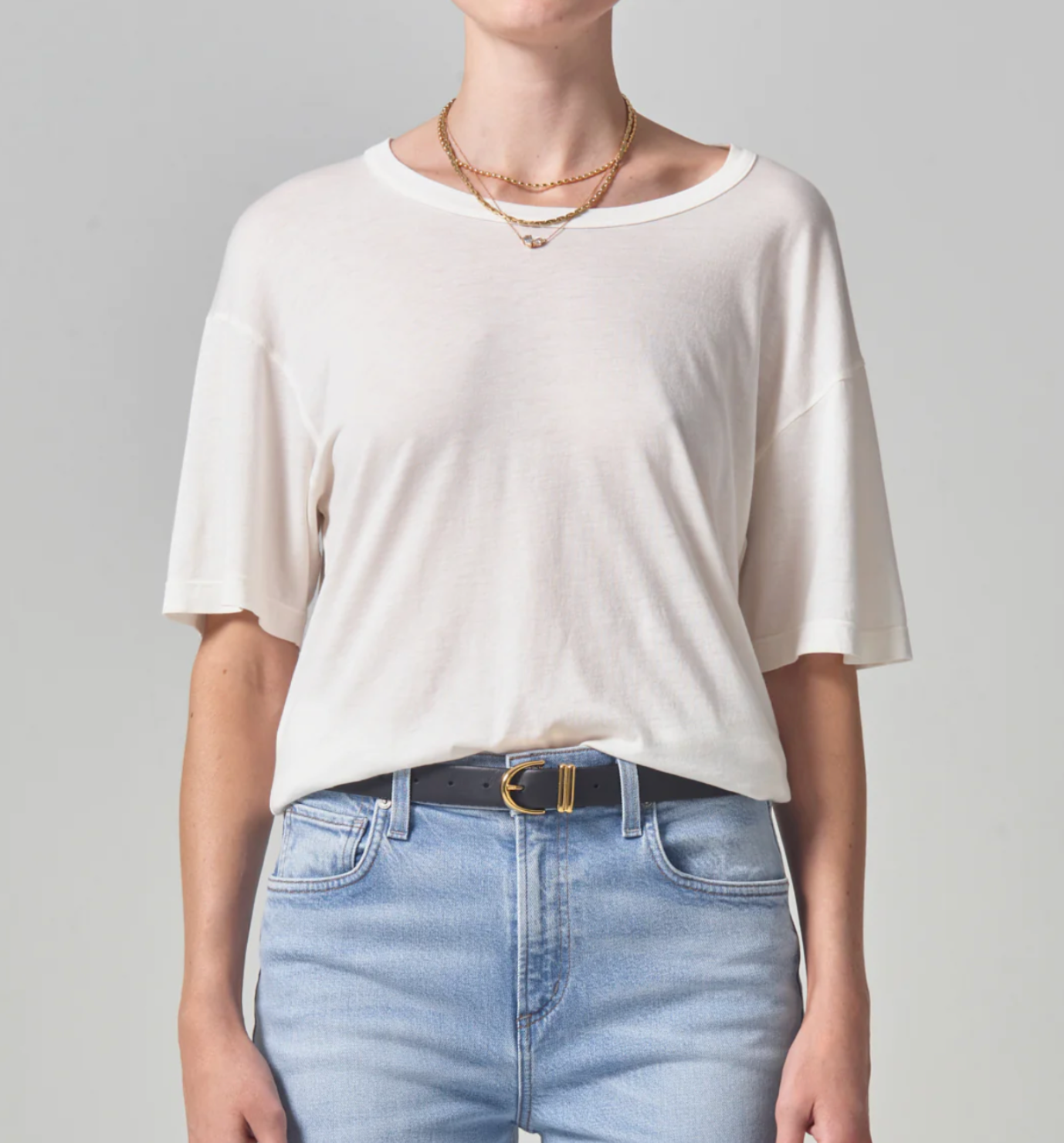 A person styled in a Citizens Of Humanity/AGOLDE Elisabetta Relaxed Tee In Pashmina and light blue jeans with a black belt, cropped at the neck so only the torso is visible. A gold necklace is also visible.