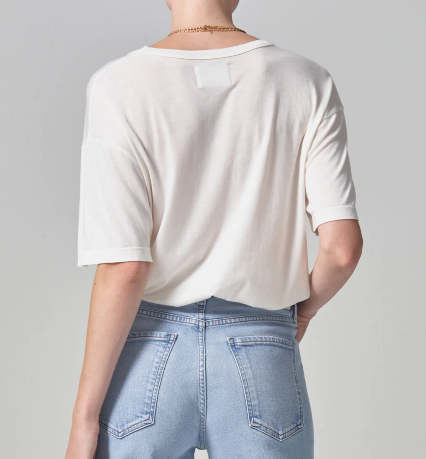Rear view of a person wearing a Citizens Of Humanity/AGOLDE Elisabetta Relaxed Tee In Pashmina and light blue jeans, standing against a light gray background. The focus is on the style of the clothes.