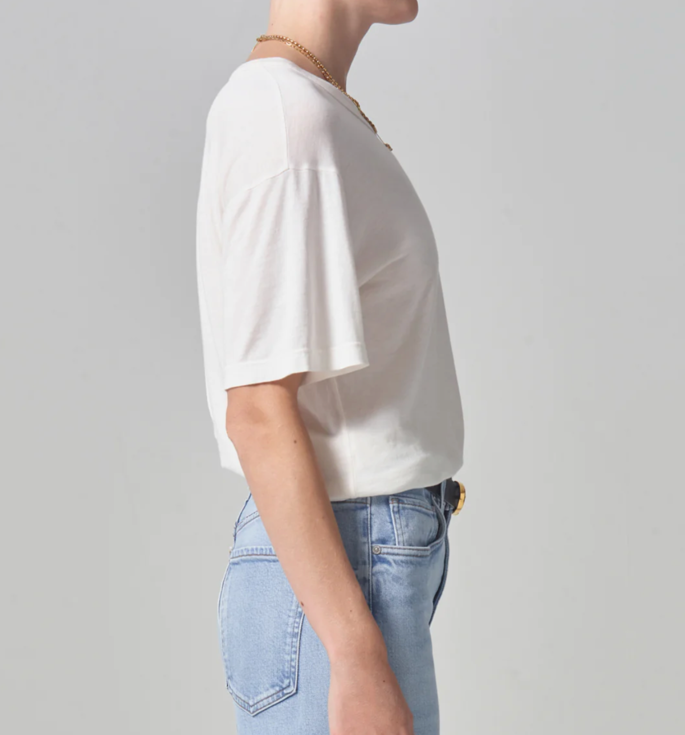 Side profile of a person wearing a Citizens Of Humanity/AGOLDE Elisabetta Relaxed Tee In Pashmina and blue jeans against a light grey background. The focus is on the Arizona style of the clothes.