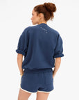 Blue cotton Clare Vivier Le Jogging Shorts with side seam pockets, modeled from the back by a woman with curly hair.