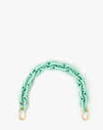 The Shortie Strap Q1 by Clare Vivier features a mint green chain with chunky links and two gold-toned clips, highlighting a vintage brass and silver charm against a white background.