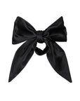 Introducing The Silk Bow by Donni: an elegant black satin accessory made from 100% silk, featuring a classic bow shape with a smooth and lustrous texture. Its two long tails and light-reflecting fabric highlight its silky finish, beautifully presented against a plain white background.