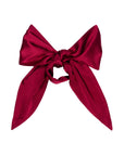 The Silk Bow by Donni is a large, deep red 100% silk accessory with wide loops and long tails, shown on a white background—perfect for elegant occasions.