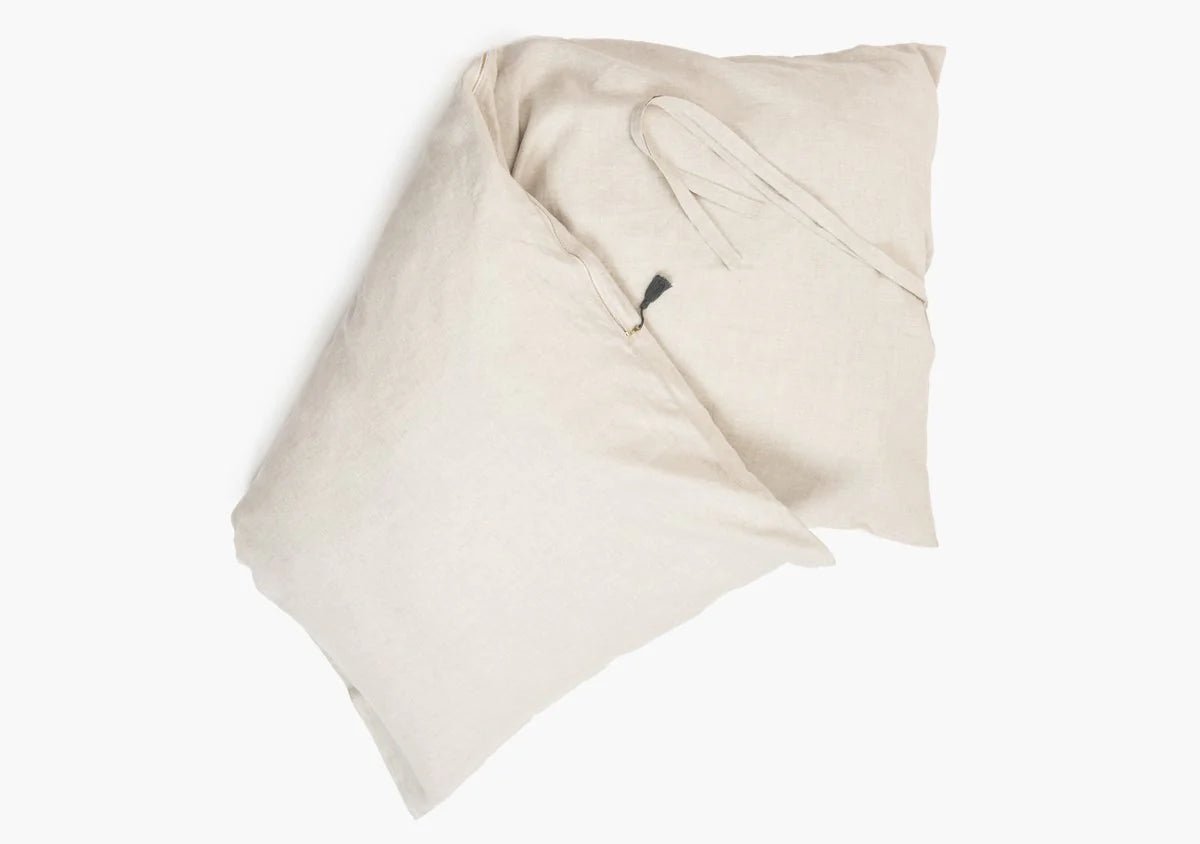Two Hedgehouse Throwbed pillows in light beige, featuring a soft texture, overlap on a white background. One pillow displays fabric ties and includes a removable cotton cover for easy cleaning.