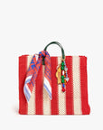 The Clare V Bandana by Clare Vivier is a red and beige striped woven tote bag with dark green handles, made in India, and adorned with a colorful cotton scarf and a beaded keychain with small charms.
