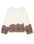 The Chariot Top is a white textured cotton long-sleeve top with a loose fit and detailed brown lace accents on the hem and cuffs.