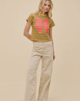 A woman poses against a beige background wearing DayDreamer's 44 Striped Vintage Tee, featuring a bold pink "44," styled with cream wide-leg pants and black shoes for a retro-inspired look.