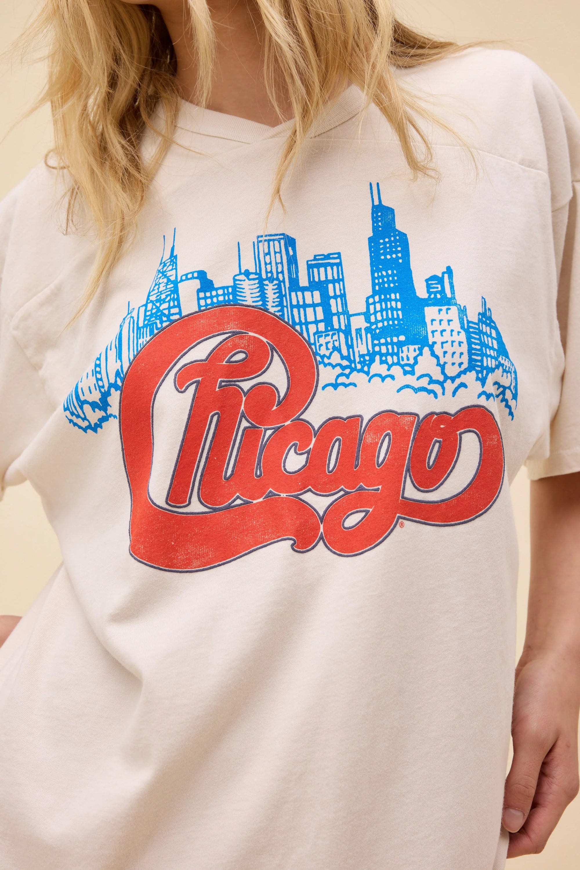 A person wearing the DayDreamer Chicago Skyline Tee sports a white shirt with a blue skyline outline, bold red cursive "Chicago," and is made from heavyweight cotton for lasting comfort.