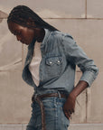 The Great Inc. Howdy Top lightweight denim shirt with pearl snaps, styled casually with jeans against a neutral wall.