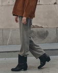The Great Inc. Fleece Sport Sweatpant styled with black boots and a brown jacket on a city sidewalk by a weathered wall.