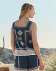 A woman with long blonde hair faces away outdoors, wearing The Sparrow Tank by The Great Inc.—a vintage-inspired blue sleeveless top with cotton crochet lace and white trim—set against hills and a clear sky.