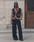 Patterned shirt and wide-leg pants by The Great Inc., modeled by a stone and metal wall, relaxed modern style.
