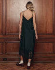 The Great Inc. black silk Legacy Dress with mesh lace, vintage-inspired, shown against a wood-paneled backdrop.