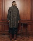 The Great Inc. The Trench Coat in a modern setting, shown by a wood-paneled wall with a stool nearby.