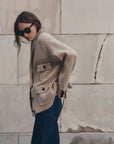 The Great Inc. Commander Riding Cardigan in blue, styled with jeans by a light stone wall for a modern casual look.