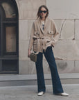 Woman outdoors in wide-leg jeans with striped handbag, styled by The Great Inc.; casual modern setting.