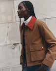 Swingy jacket with red collar by The Great Inc., styled with braids beside a textured stone wall.