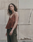 The Great Inc. Port Cami in green, styled with matching pants against a rustic stone wall backdrop.