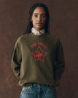 A woman with braids wears The College Sweatshirt by The Great Inc., featuring a bold Wild Panther graphic.