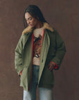 A woman wearing The Quilted Liner Parka by The Great Inc., featuring a green quilted design and removable faux fur collar.