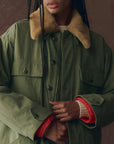 A person with dreadlocks wears The Quilted Liner Parka by The Great Inc., a green vintage-inspired military jacket with a removable faux fur collar.