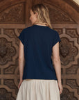 A blonde woman stands with her back to the camera in front of an ornate Los Angeles wooden door, wearing The Boxy Crew w/ Everglade Graphic by The Great Inc. and a cream skirt.