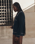 The Great Inc. menswear-inspired tipping polo and plaid skirt in natural light by a window with metal bars.