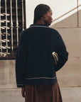 The Menswear Tipping Polo by The Great Inc., styled with a plaid dress and dark jacket, modern and chic look.