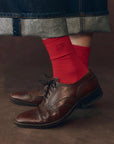 Bright red cotton The Great Inc. Monogrammed Trouser Socks styled with brown dress shoes and cuffed jeans.