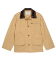 The Great Inc.'s Barn Jacket is a tan, garment-dyed cotton workwear jacket with brown buttons, utility pockets including a zip chest pocket, a dark brown leather collar, and an inner label for a casual yet structured look.
