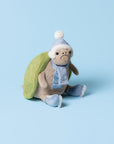 Timmy Turtle Skating by Jelly Cat Inc. is a festive plush turtle with a green shell, blue winter hat, scarf, and boots, ready for icy fun. He sits cheerfully on a light blue background.