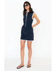 A woman wears Kule's The Terry Dress, a chic, sleeveless navy blue dress featuring a stylish zipper closure and white trim. She complements her look with sunglasses and casual flip-flops while standing against a plain white background.