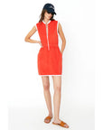 A person is wearing The Terry Dress by Kule, a chic sleeveless red dress with a front zipper, white trim, and pockets. It's paired with a black cap, sunglasses, and brown slide sandals against a plain white background.