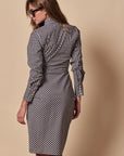 A woman wearing sunglasses and The Wrap Front Dress by THE SHIRT, featuring black-and-white checks and long sleeves, stands with her back to the camera against a plain beige background.