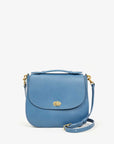 The Turnlock Louis w/ Top Handle by Clare Vivier is a blue leather handbag made from vegetable-tanned Italian leather. It features a curved flap, gold hardware with a magnetic twist lock, an adjustable crossbody strap, and a small top handle against a plain white background.