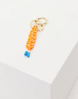 The Upside’s LIMITLESS KEYRING features a gold charm with a star and an orange macrame paracord braid, finished with blue tips, shown on a white geometric block.