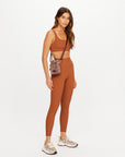 The Upside JAVAN LILO rust crossbody bag styled with athleisure outfit, shown on white background.