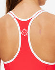 The image shows the back of a person wearing The Upside PACIFIC ALI RACER BACK DRESS in red with white trim, featuring moisture-wicking fabric and a small white geometric logo between the shoulder blades.
