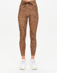 A person models The Upside PANTHERA 25IN MIDI PANT—high-waisted, ankle-length, brown leopard print leggings with moisture-wicking fabric and white sneakers. Only the lower body is visible against a plain white background.