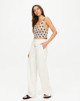 A woman poses against a white background wearing The Upside's BOW N ARROW NOVA FLARE PANT and a floral crop top with spaghetti straps, paired with black sandals.