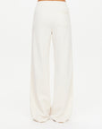 A person in The Upside's BOW N ARROW NOVA FLARE PANT, off-white, high-waisted and loose-fitting with a single back pocket, stands against a plain white background.