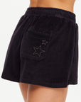 A close-up of a person wearing The Upside SADDLE UP ZIGGY SHORT—black terry towelling gym shorts featuring an elastic waistband and a back pocket with two star-shaped embroidered designs.