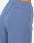 Close-up of a person wearing The Upside SIERRA PANT in light blue recycled polyamide, featuring an elastic waistband, side pocket, and two small black arrow graphics near the waistband.