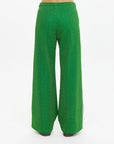 A person stands with their back to the camera in The Upside's GALAXIA LORETTA PANT, crafted from Amazon Green sparkle fabric, set against a plain white background.