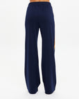 A person faces away, wearing The Upside’s VITESSE MARNIE WIDE LEG PANT in navy blue with recycled fabric, an elasticated waistband, and a touch of orange on the side. The background is plain white.