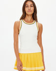 A woman faces forward against a white background, wearing The Upside's KIRSTY RIB TANK TOP with black and yellow trim, paired with a yellow pleated skirt featuring white stripes near the hem.