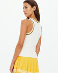 A woman poses against a plain white background, wearing The Upside's KIRSTY RIB TANK TOP—sleeveless with black and yellow trim—paired with a pleated yellow skirt featuring white striped hems.