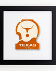 Framed artwork featuring a vintage orange and white Texas Longhorns football helmet logo with the word "TEXAS" below it. The logo is slightly worn, adding a nostalgic feel to the piece. The black frame, paired with a white background, beautifully highlights the print's graphic design. This piece is called Art Square Blk Frame by Match South.